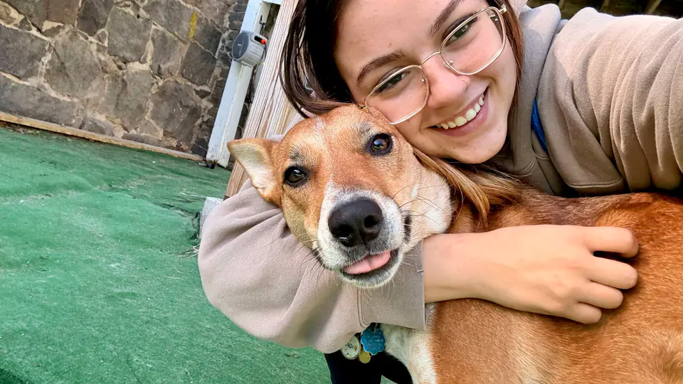 Staff member hugging a grinning shepherd mix on the turf