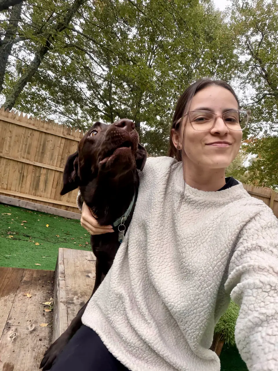 Staff selfie with a chocolate lab in the outdoor yard