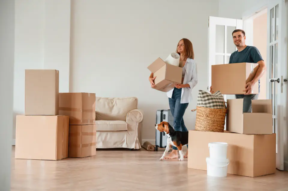 Walking forward with boxes. Young couple with dog are moving