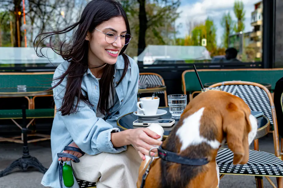 A young woman calmly petting her beagle at an outdoor cafe table