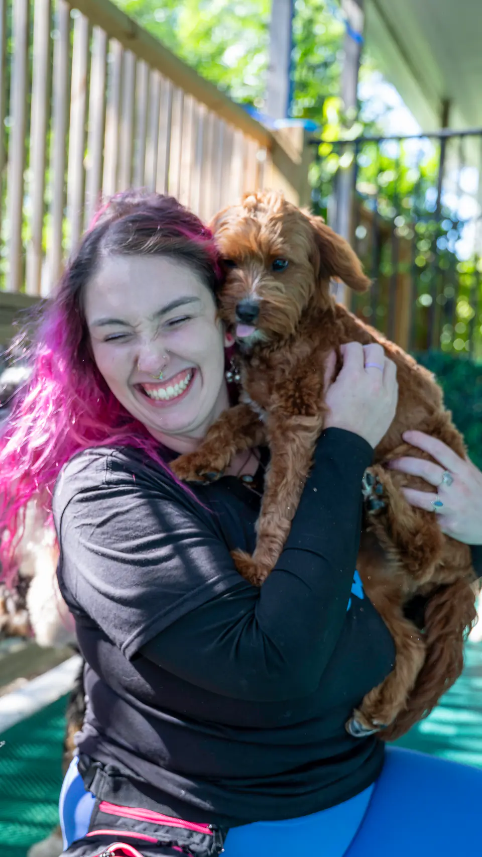 Una persona del equipo de adiestramiento de Dogtown abraza a un cachorro doodle de pelo rojizo.